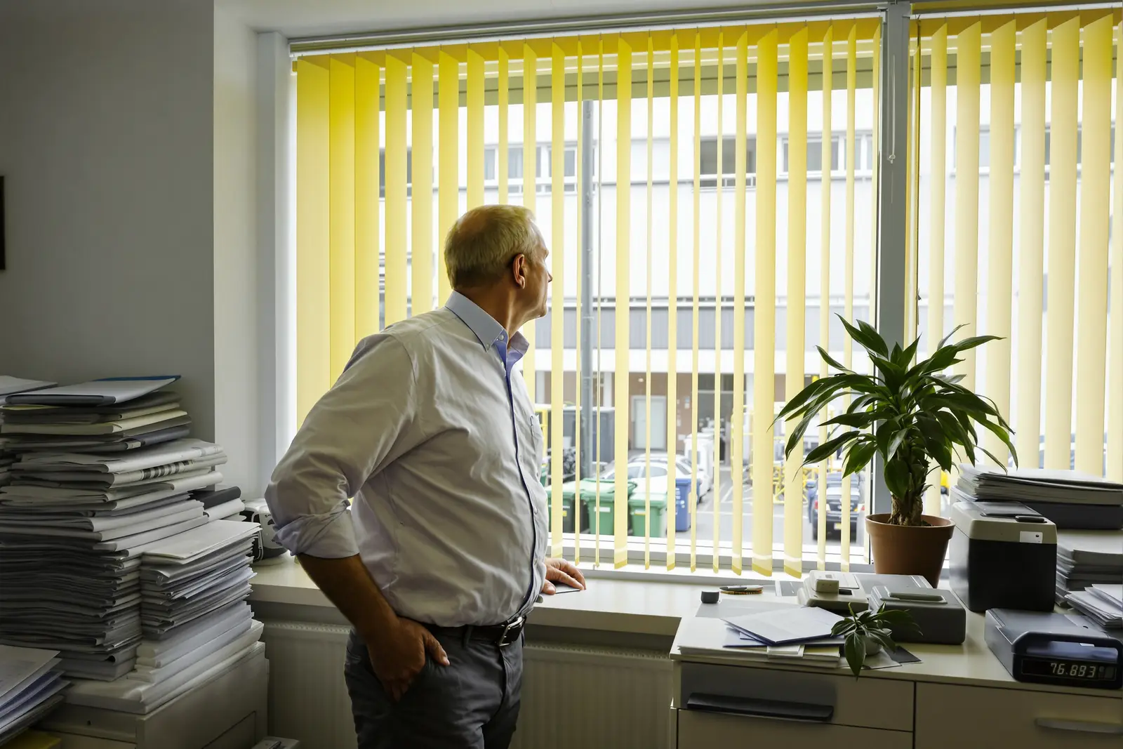 Man in an office between stacks of files looks out the window, asking how to find meaning in his work