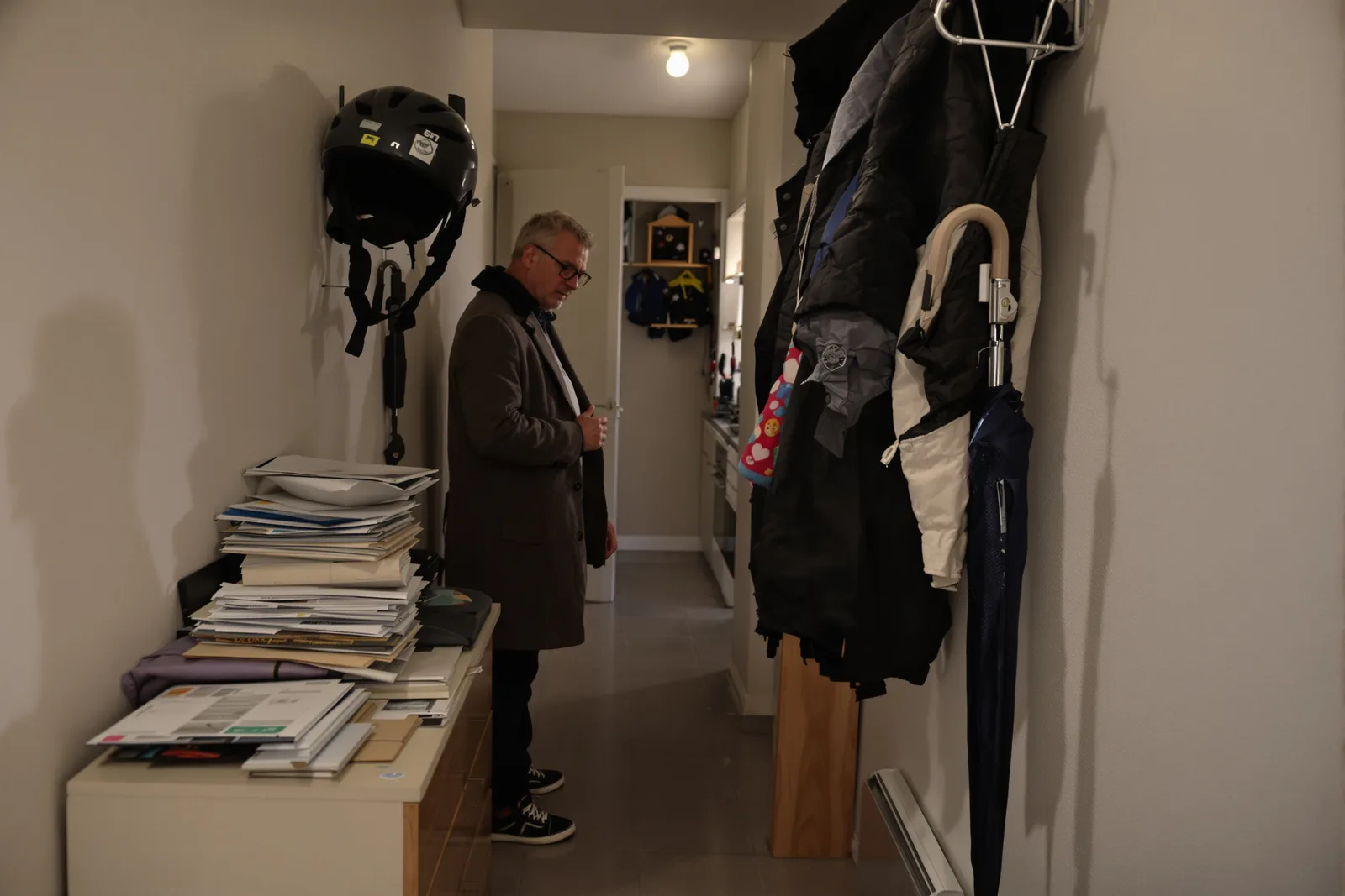Man in a coat stands in a hallway at night by a pile of post, the moment the inner critic often gets loud