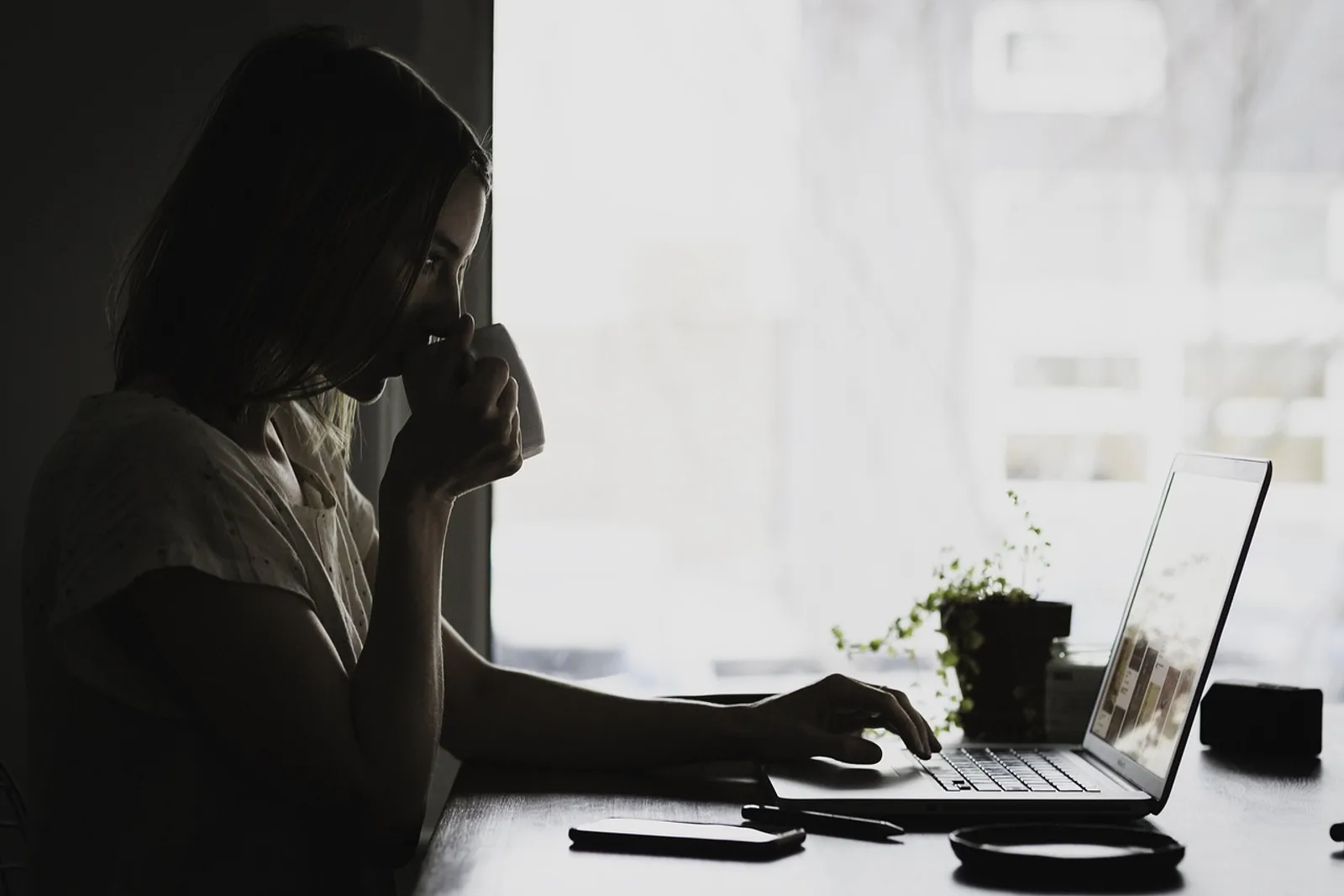 Woman pausing at her desk in morning light, the first step in learning how to stop feeling like a fraud at work
