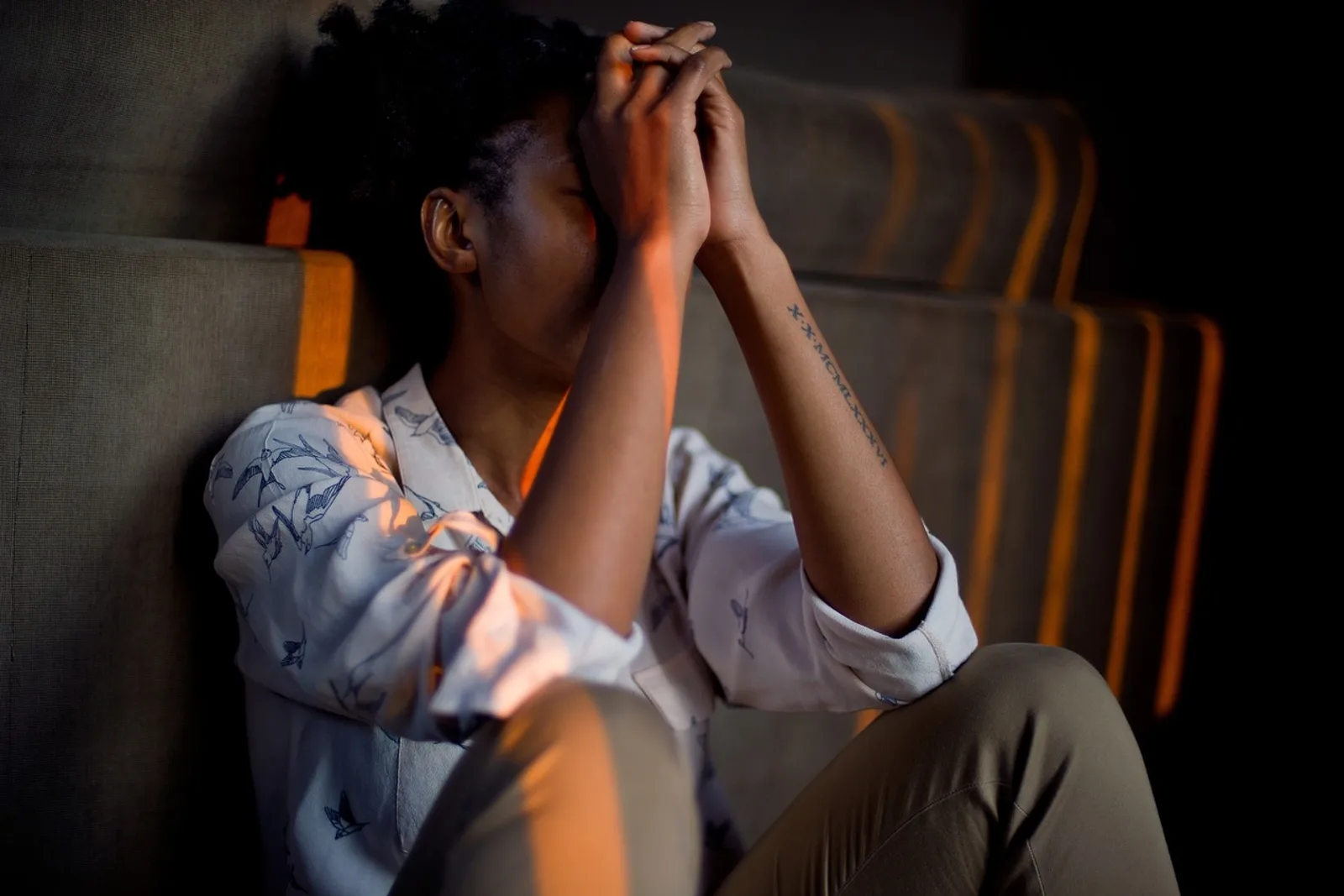 Woman on the floor leaning against a sofa, hands on her forehead, asking why she fears abandonment