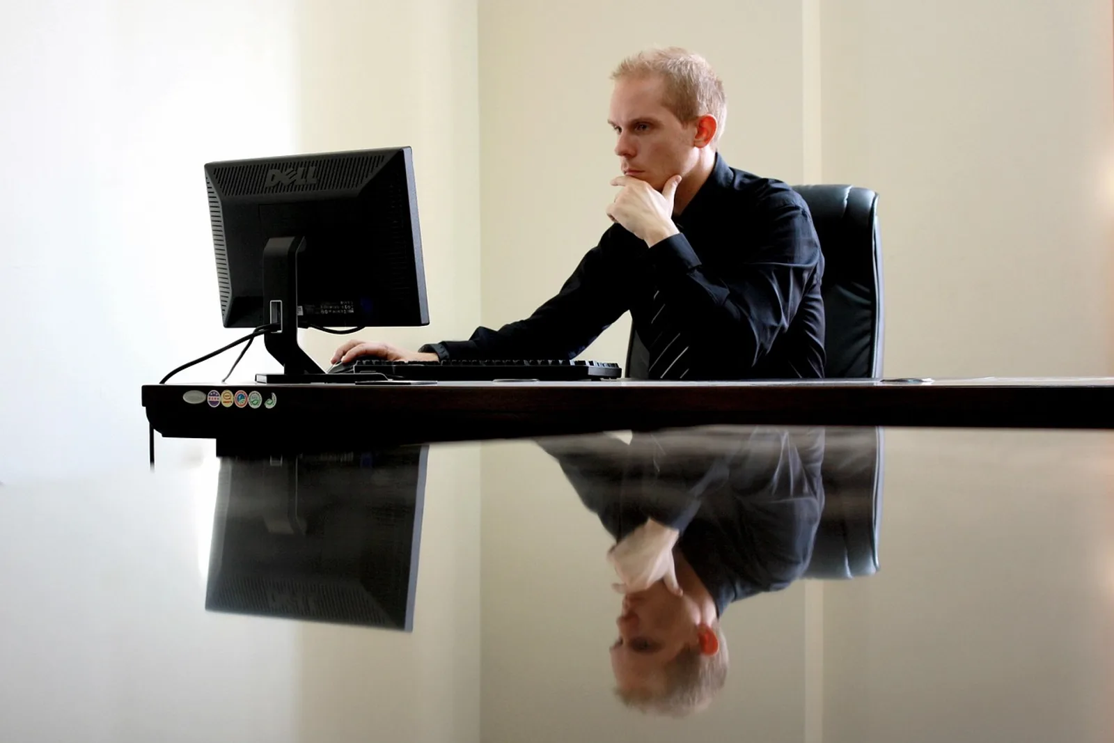 Unternehmer denkt mit der Hand am Kinn vor dem Monitor nach, ein typischer Moment für Business Hypnose im Büro