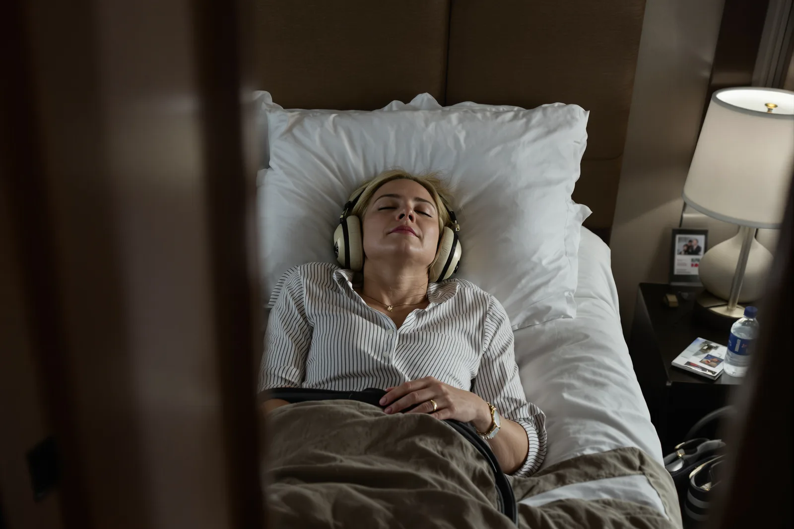 Frau liegt mit geschlossenen Augen und Kopfhörern im Bett und hört ein Hypnose-Audio zur Entspannung