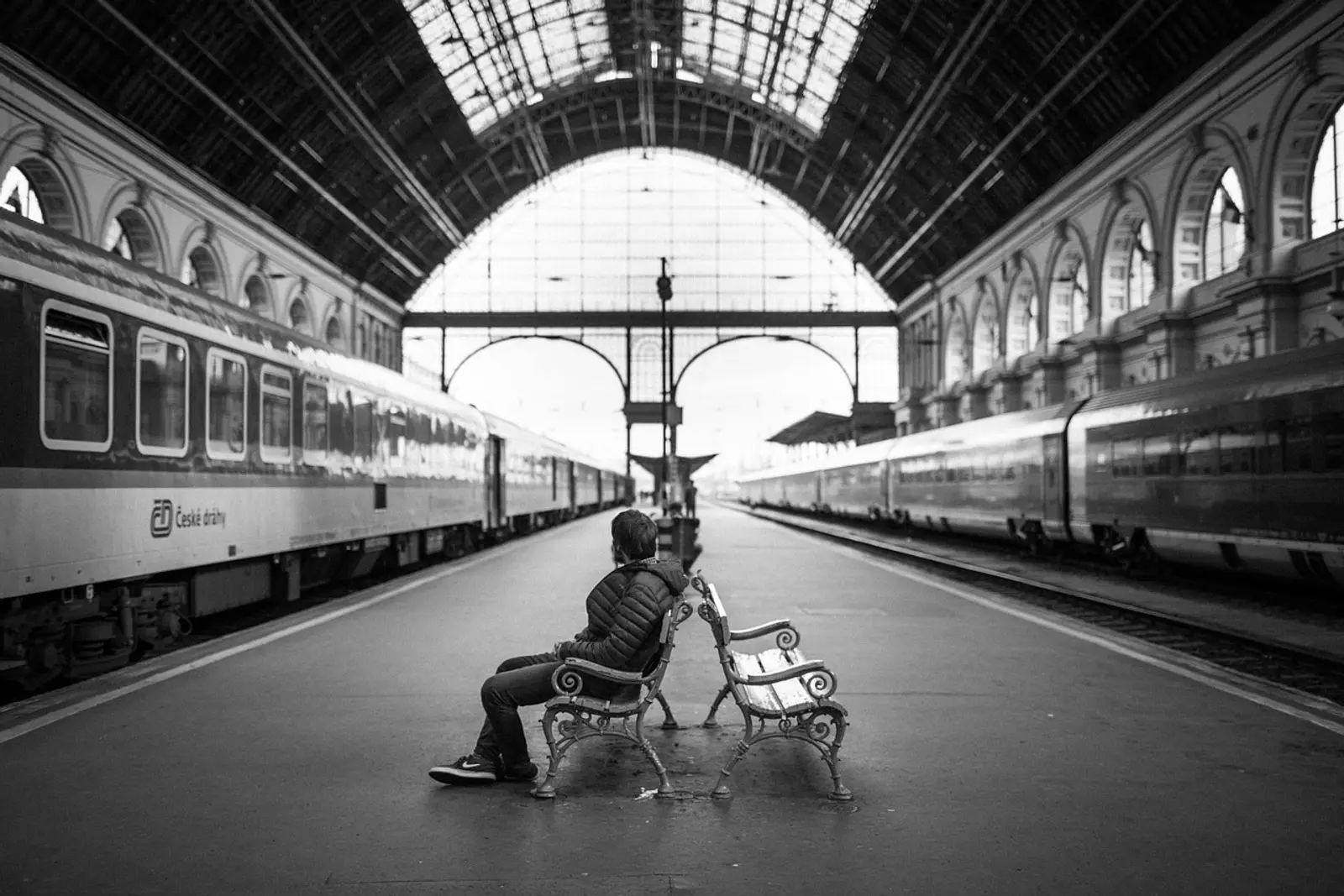 Man sitting alone on a bench on the platform of a large train station, finding calm with self-hypnosis for anxiety