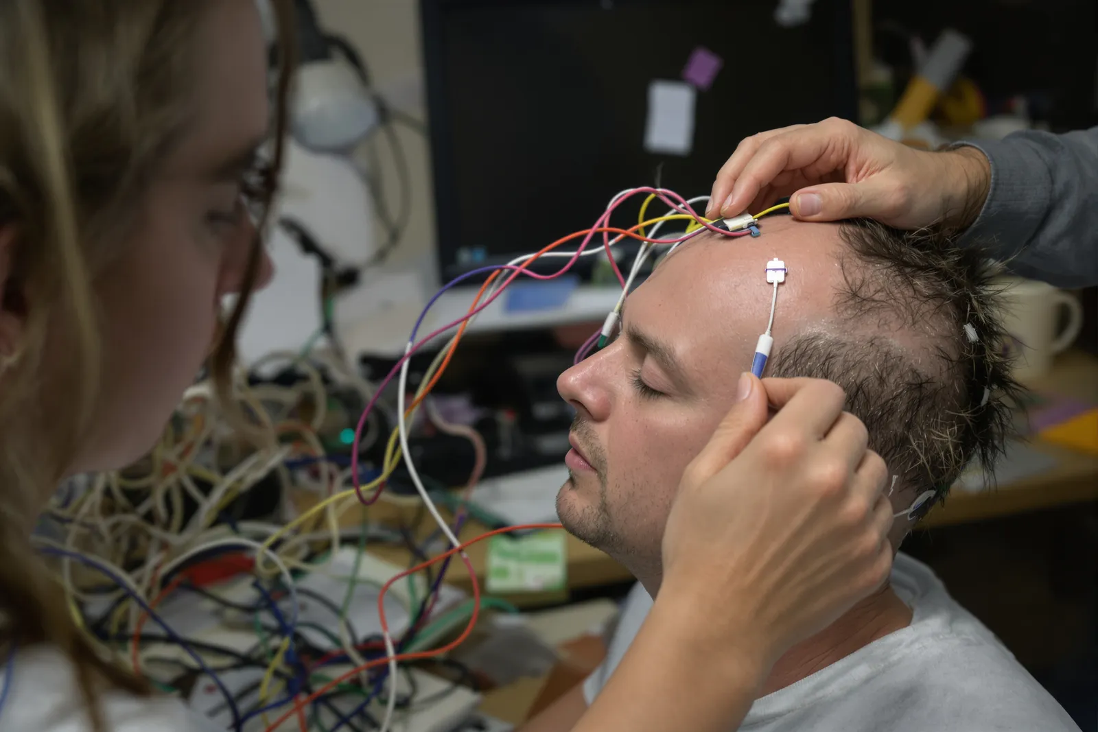 Forschende setzen einem Studienteilnehmer mit geschlossenen Augen EEG-Elektroden – Hirnmessung zur Frage: Was ist Hypnose?