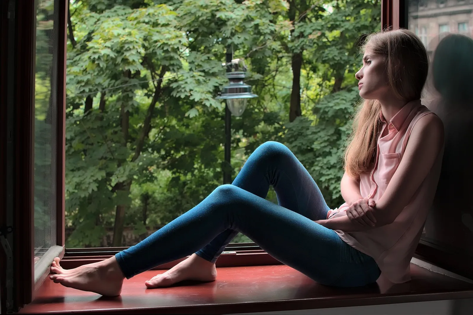 Frau sitzt entspannt und wach mit geschlossenen Augen am Fenster – Hypnose-Mythen im Faktencheck