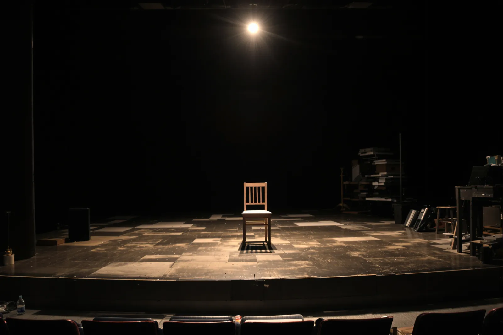 Leerer Holzstuhl im Scheinwerferlicht auf dunkler Theaterbühne als Sinnbild für den Mythos Bühnenhypnose – was ist Hypnose wirklich?