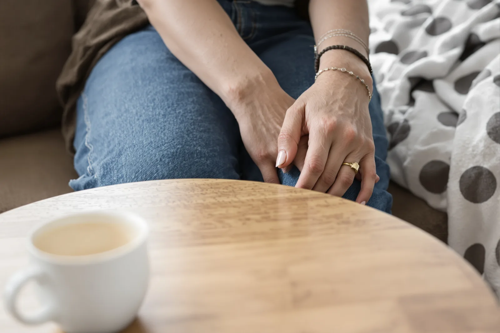 A woman’s hands resting calmly on her knee next to a cup, a quiet start to self hypnosis step by step