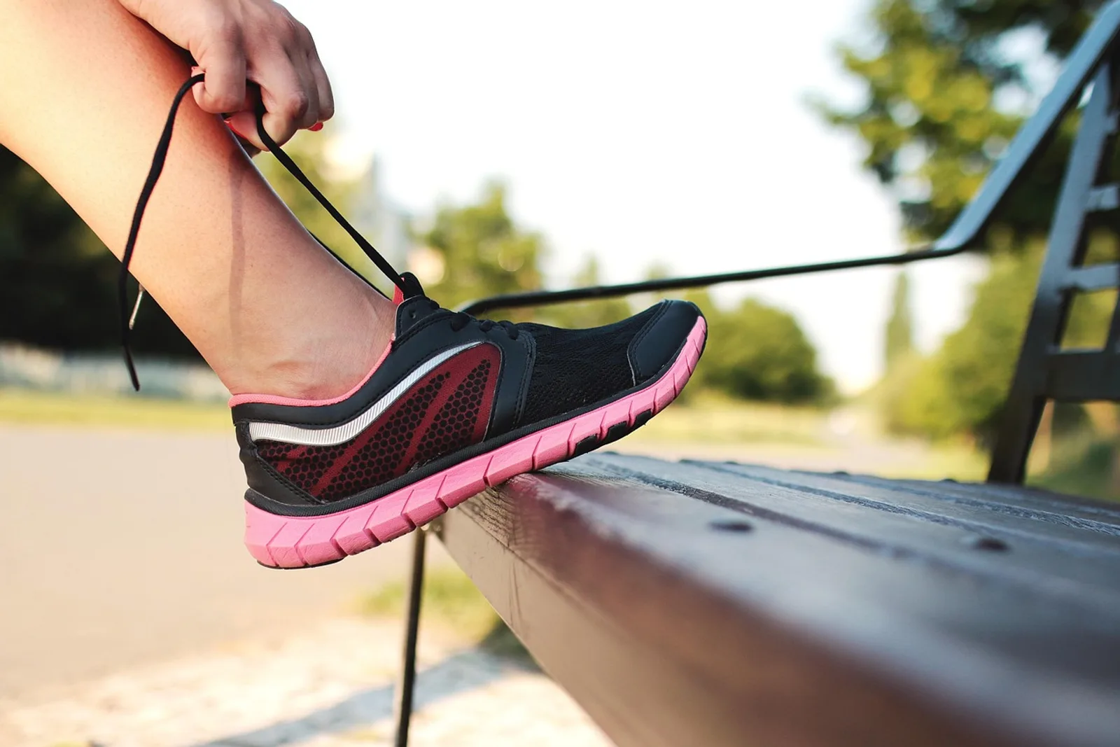 Frau schnürt auf einer Parkbank ihren Laufschuh – ein Wenn-Dann-Plan wird vor dem Lauf umgesetzt