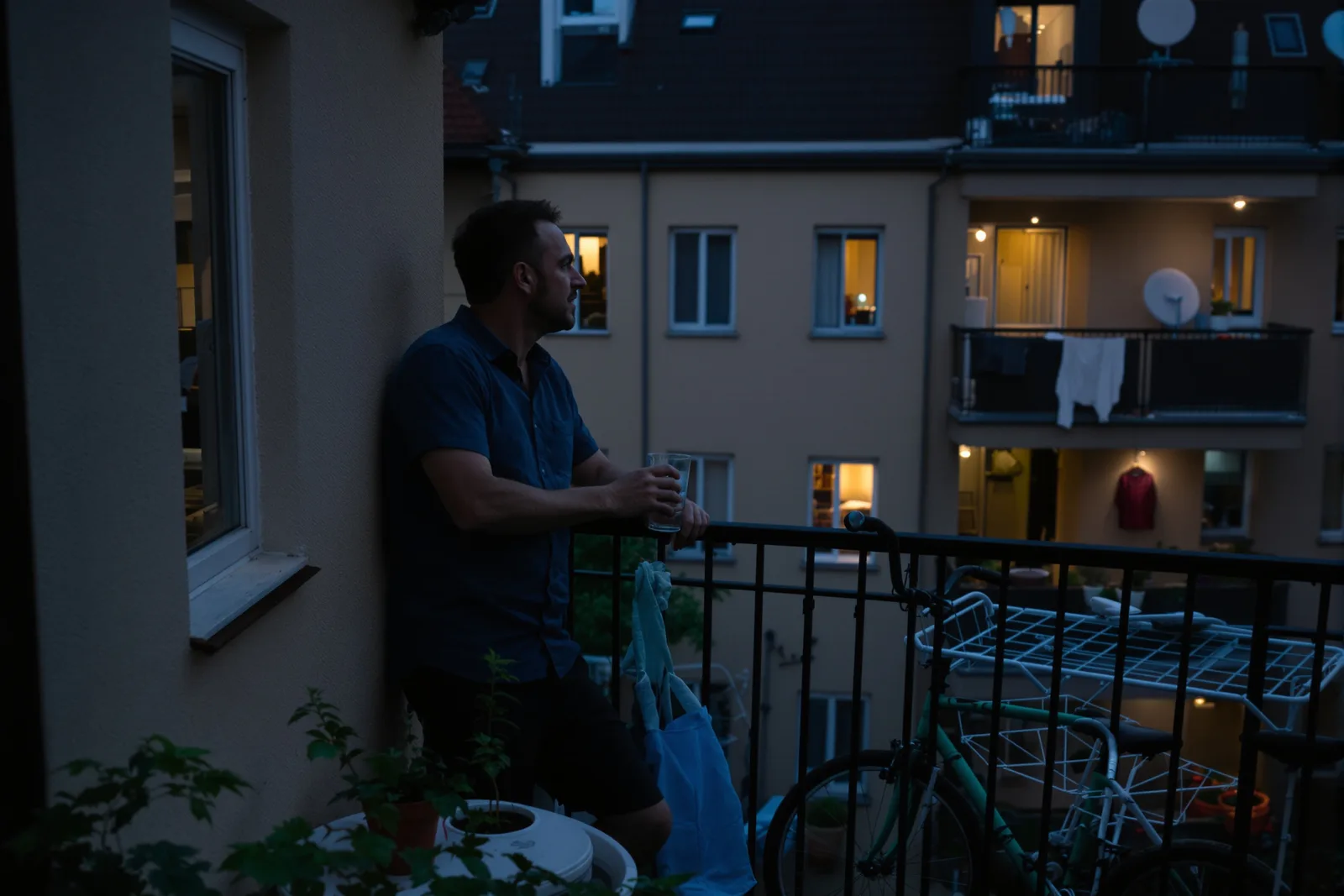 Mann steht abends mit einem Glas Wasser auf dem Balkon und atmet durch – kurzer Ausstieg bei Reizbarkeit
