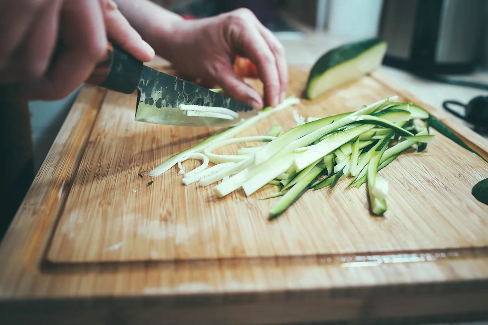 Hands slicing zucchini into strips on a wooden board, a daily routine to rebuild self esteem after a breakup